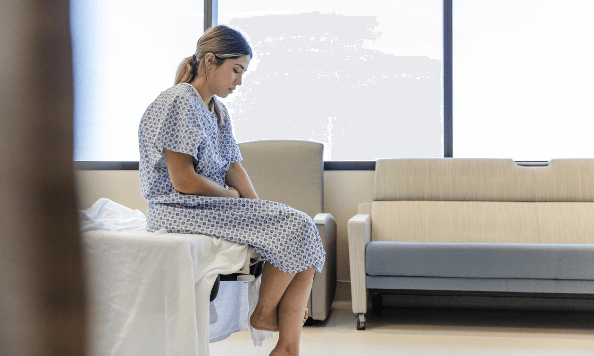 Woman in hospital gown sitting on bed