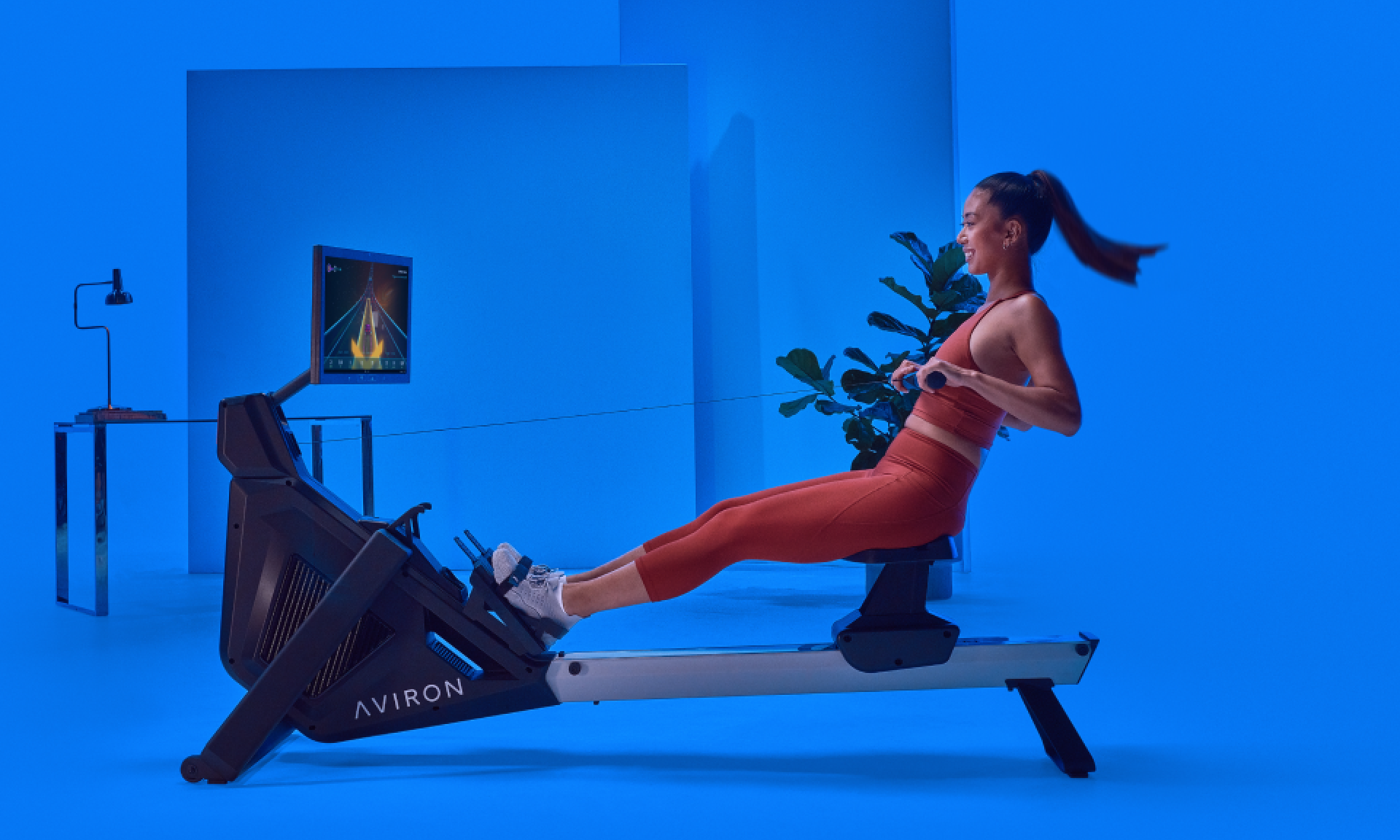 A woman rowing on the Aviron Strong Rower in a room with blue walls