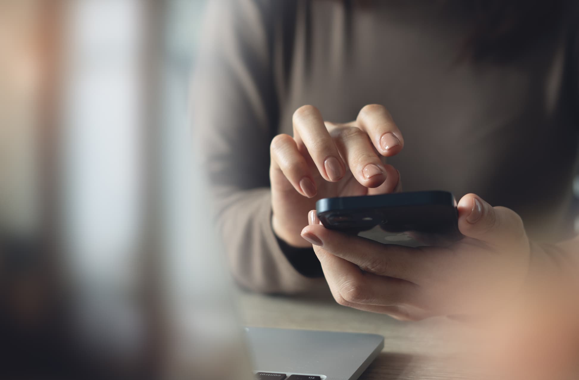 Close up, woman using mobile phone with laptop computer on office table.
