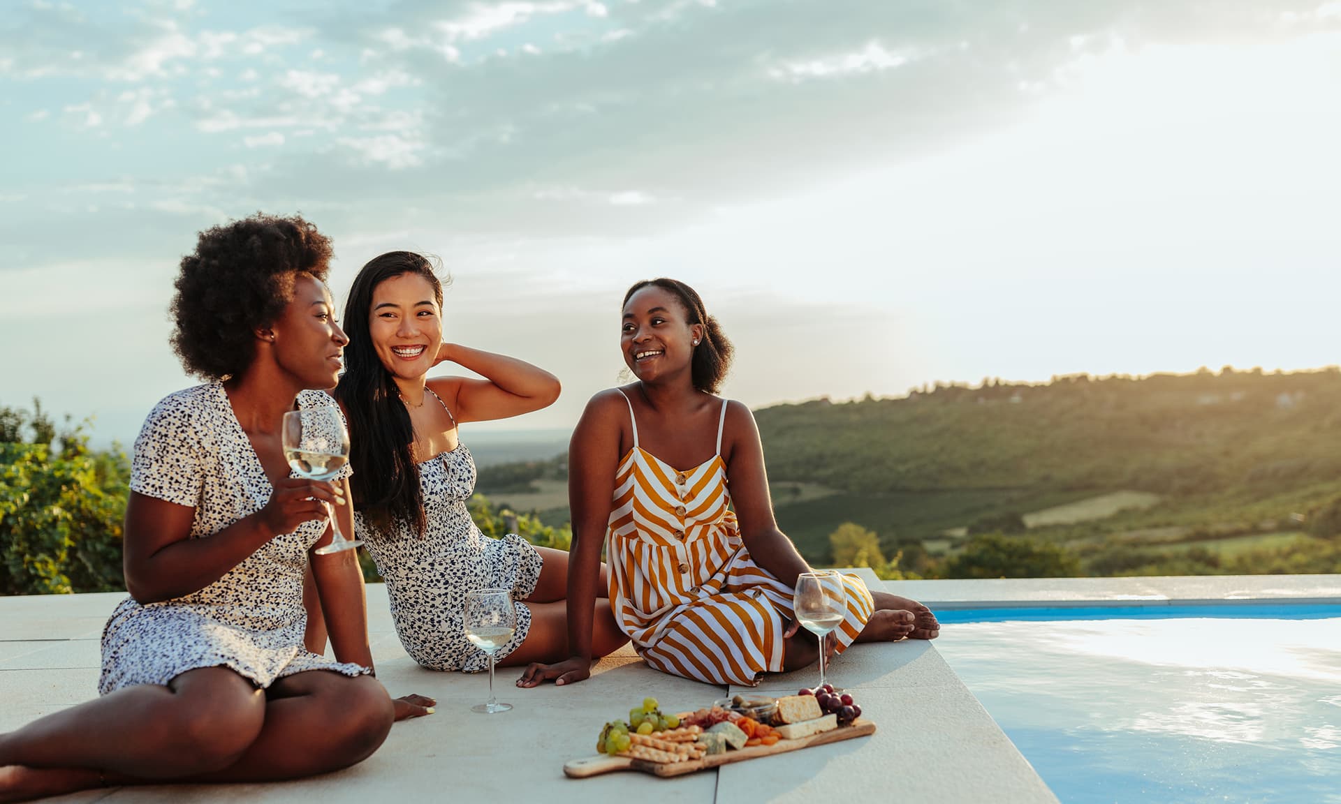 Three friends sitting by a pool and drinking wine