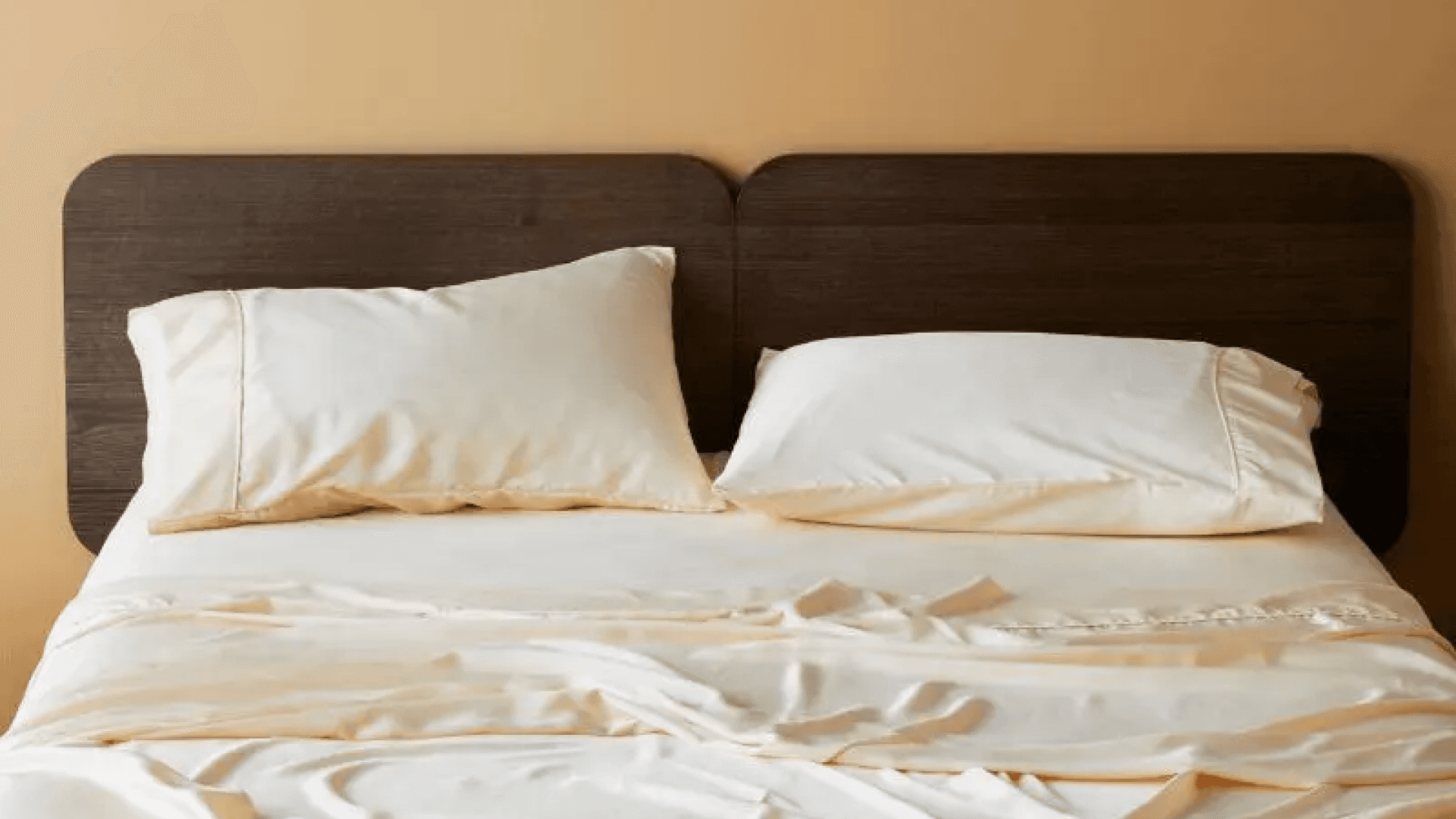 Cream sateen sets on bed with dark wooden headboard