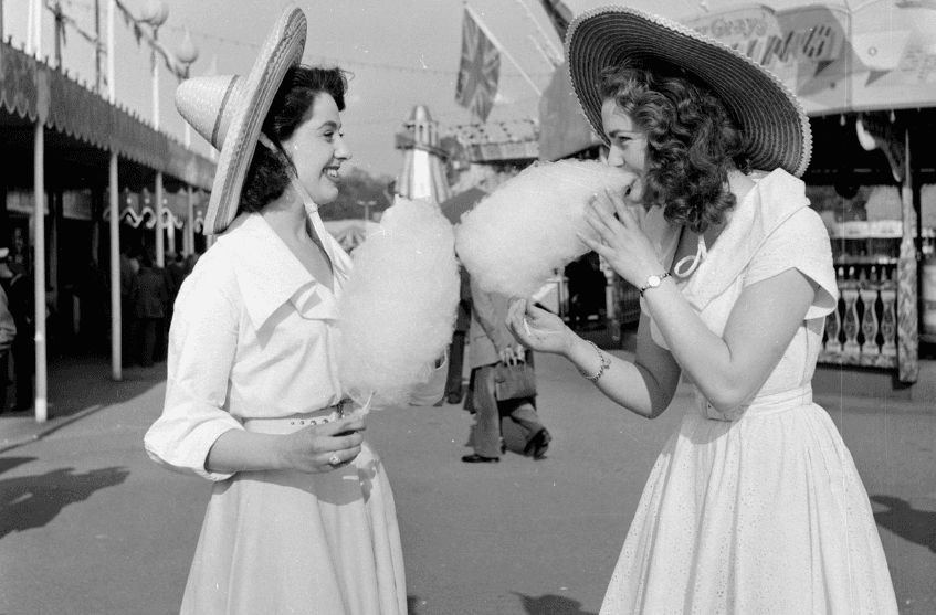 20th June 1953: Two young women eating candy floss at a fun fair in Battersea Park, London.