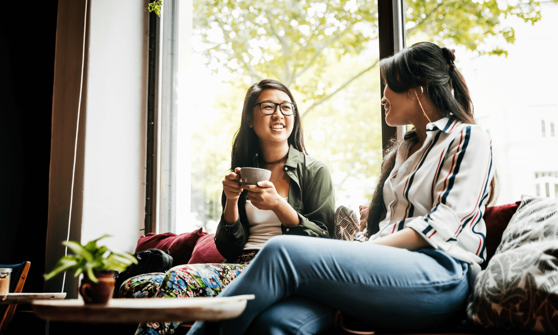 Two friends sitting on a bench in a coffee shop.