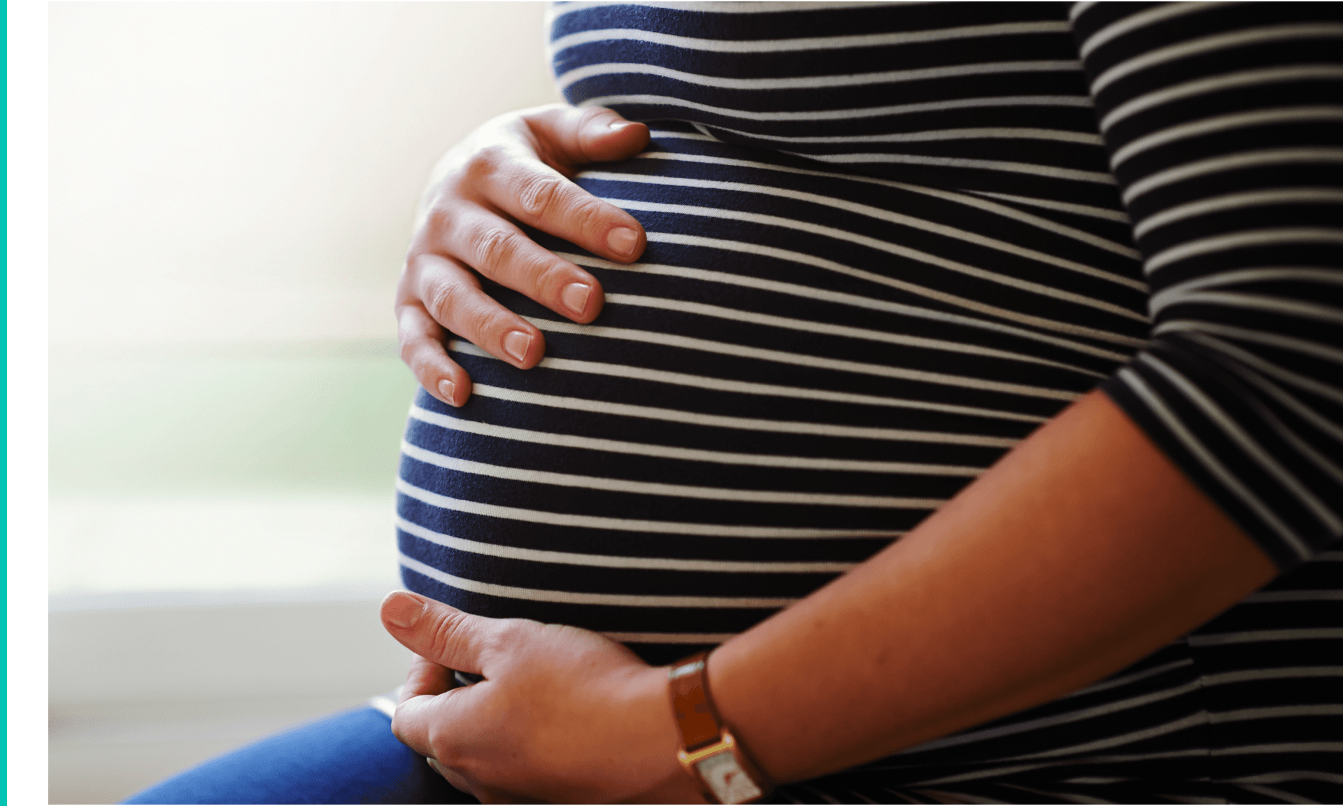 Heavily pregnant female sitting by window, holding her bump with both hands.