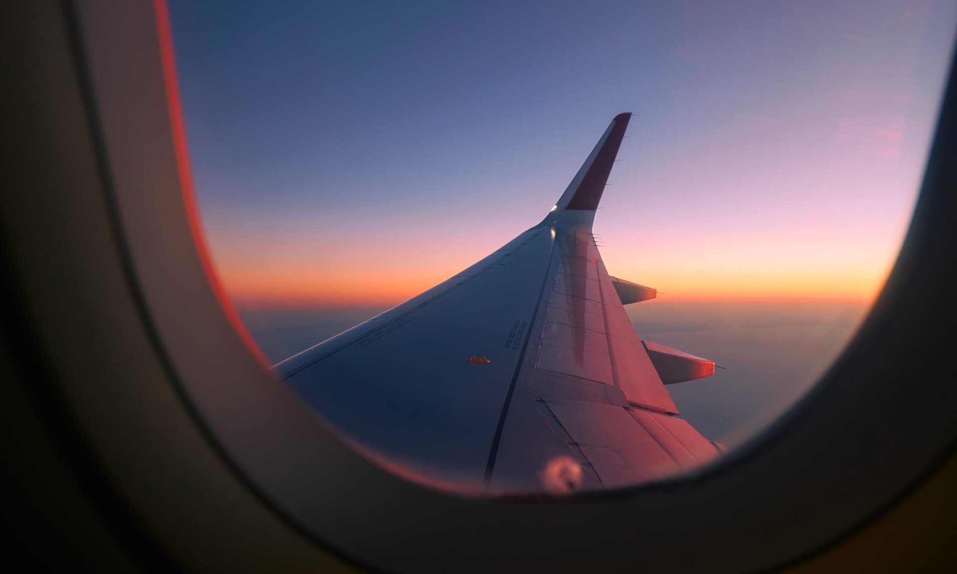 The wing of a plane looking out a window during sunset