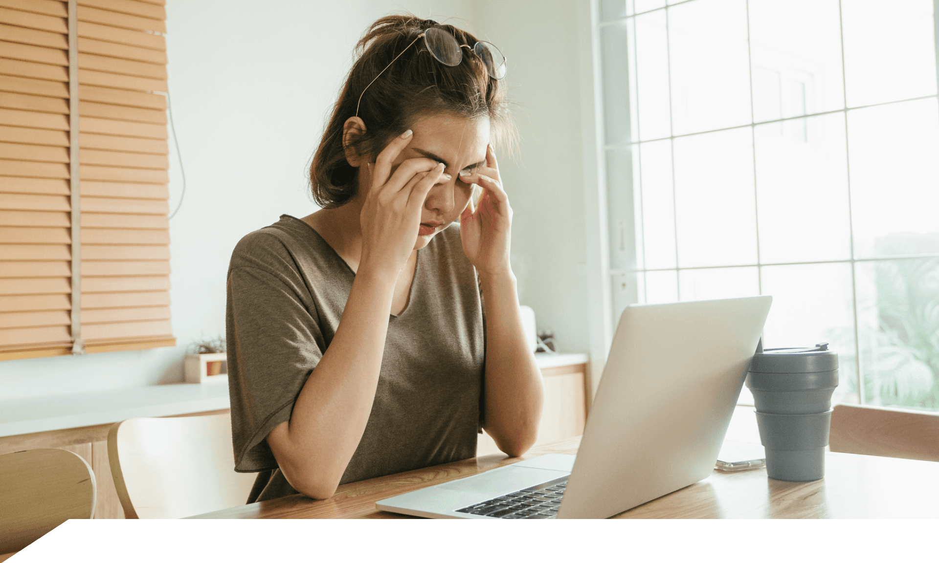 A woman sitting at her laptop covering her eyes with her hands
