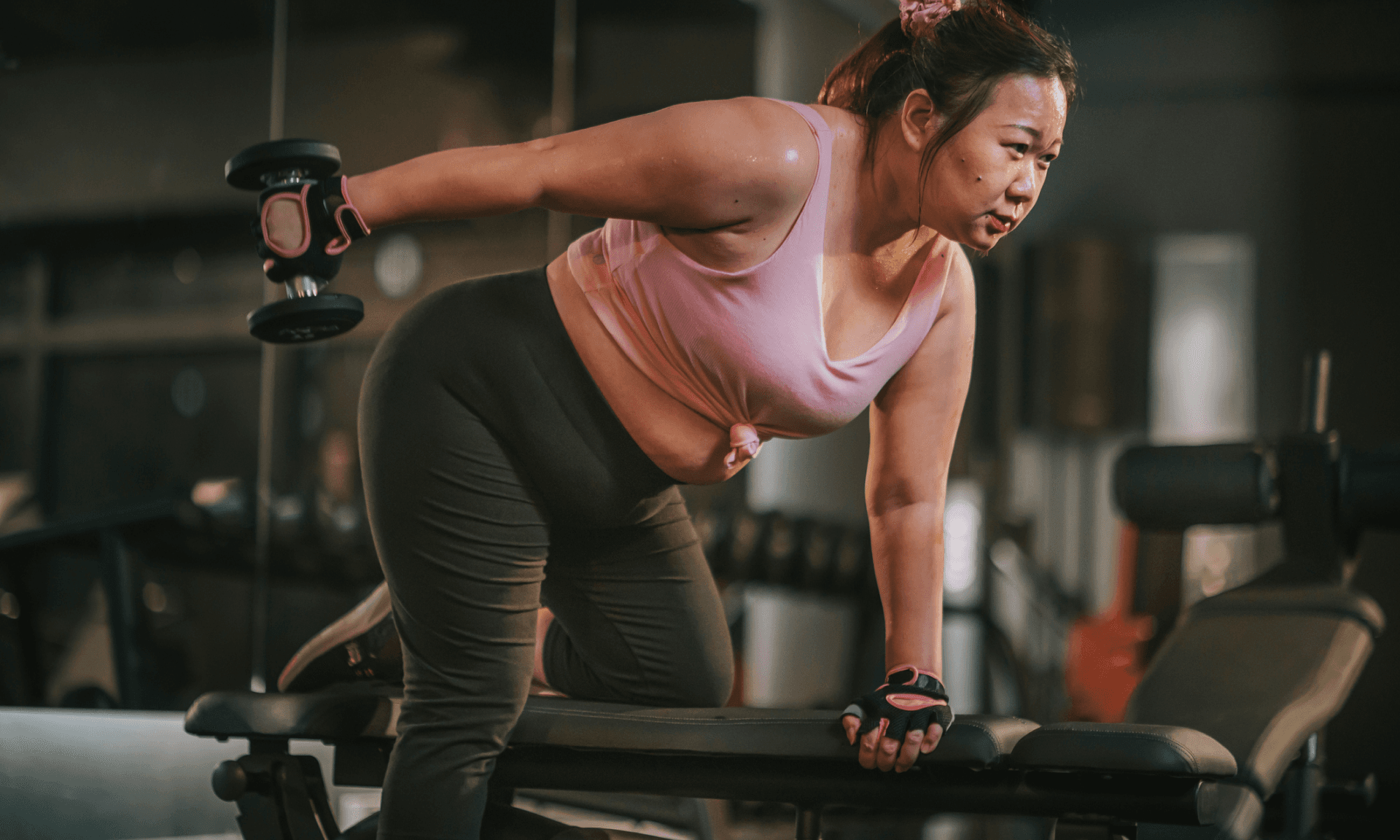 A woman bent over a bench in a gym lifting weights
