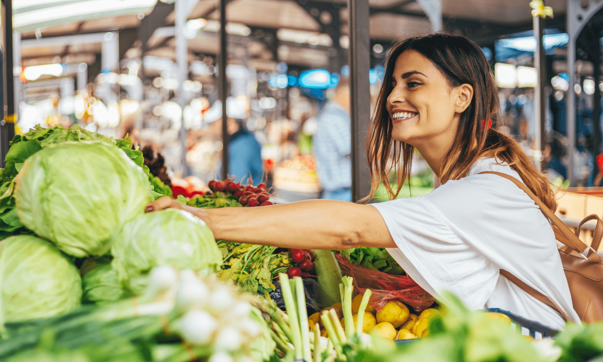 A woman smiling and reaching for cabbage at a supermarket