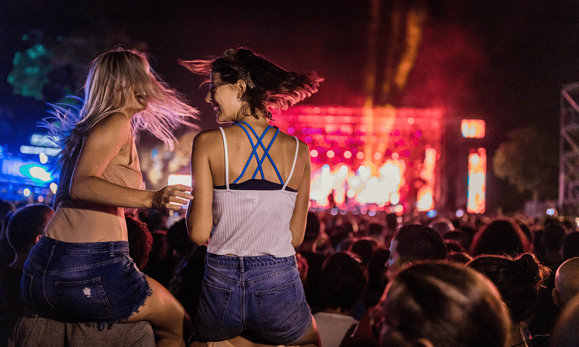 Two women sitting on shoulders at a concert
