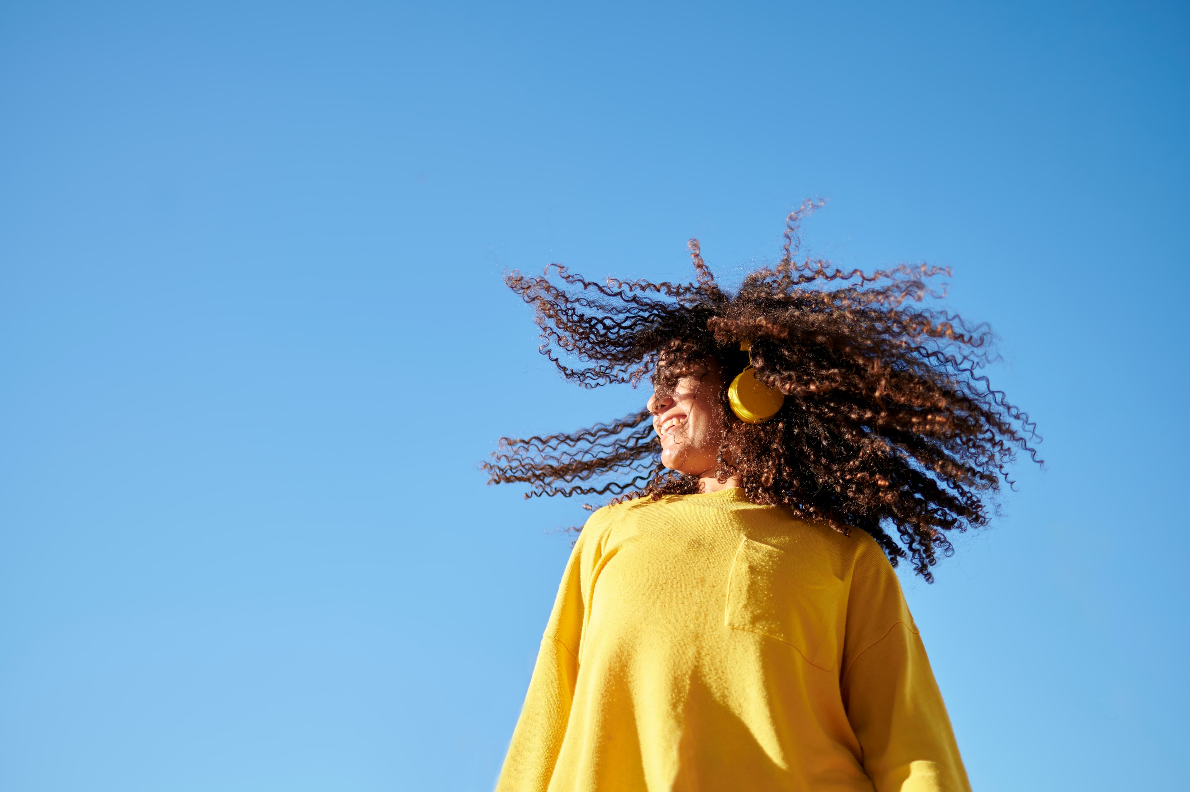 Woman moving her curly hair listening to headphones.