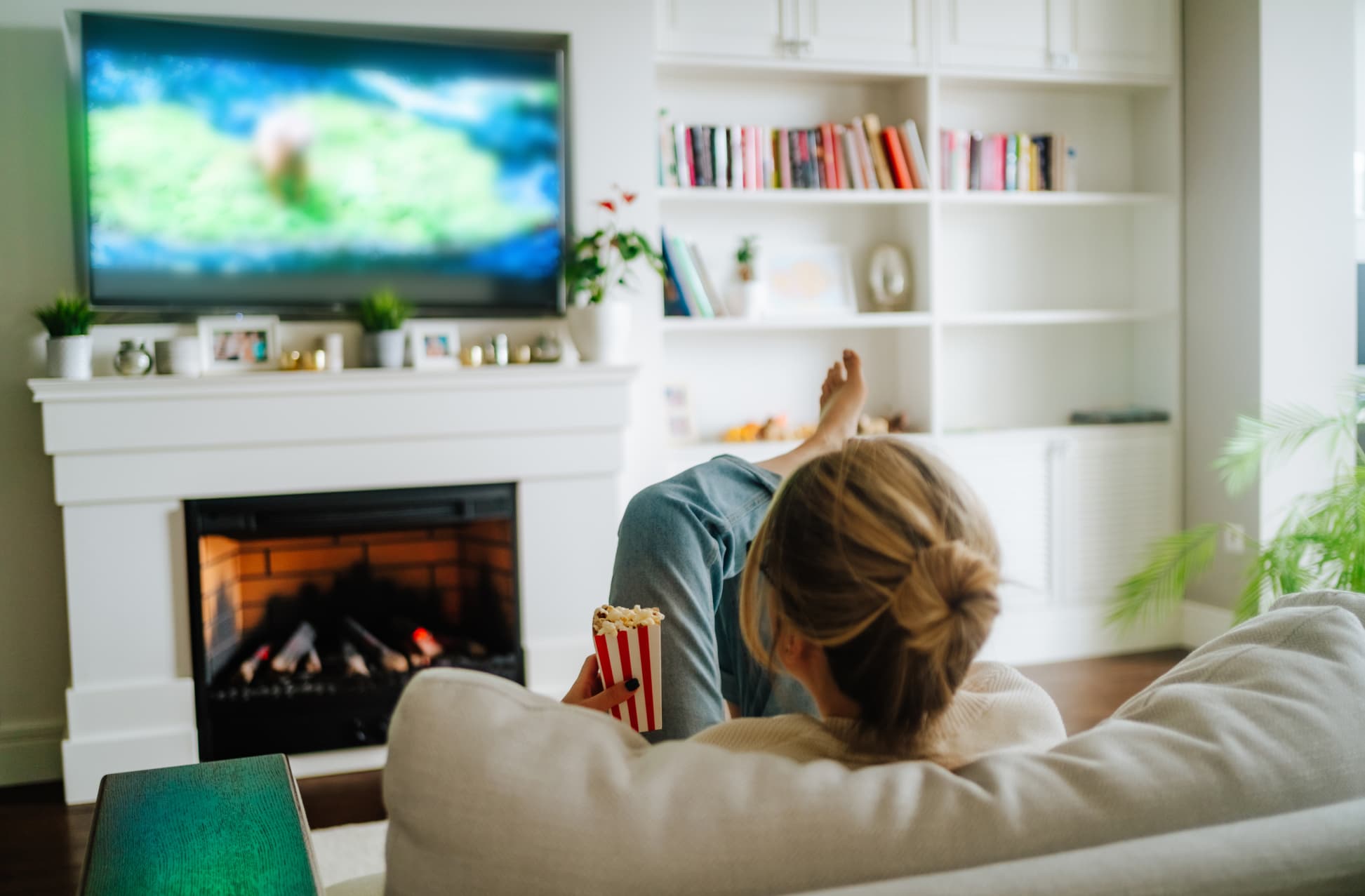 Woman eating popcorn and watching tv on a big screen at home