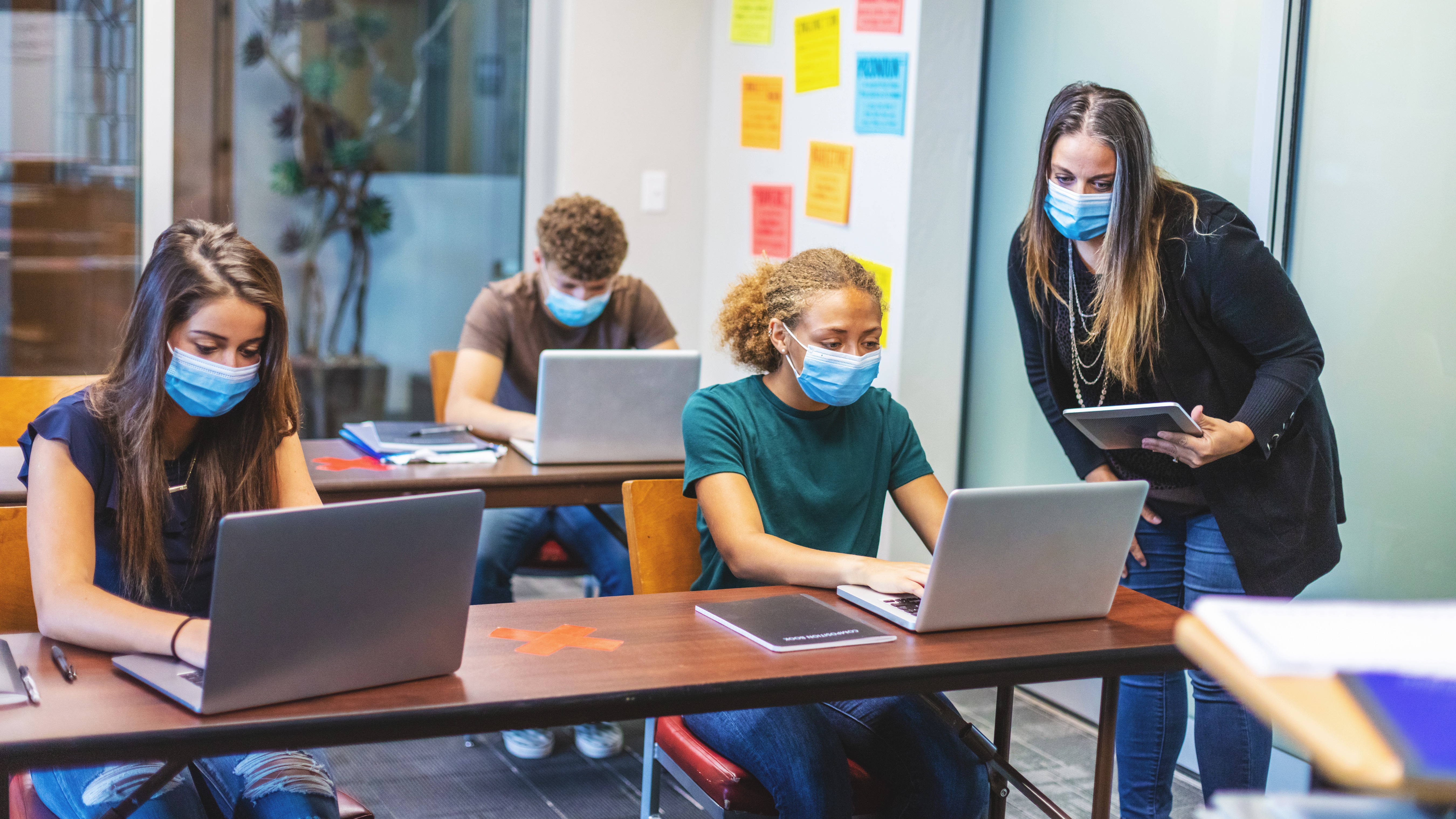 A high school teacher offers assignment assistance with three students in the classroom.