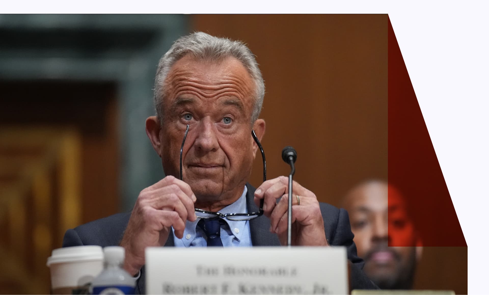 RFK Jr giving testimony before the Senate Finance Committee and holding his glasses