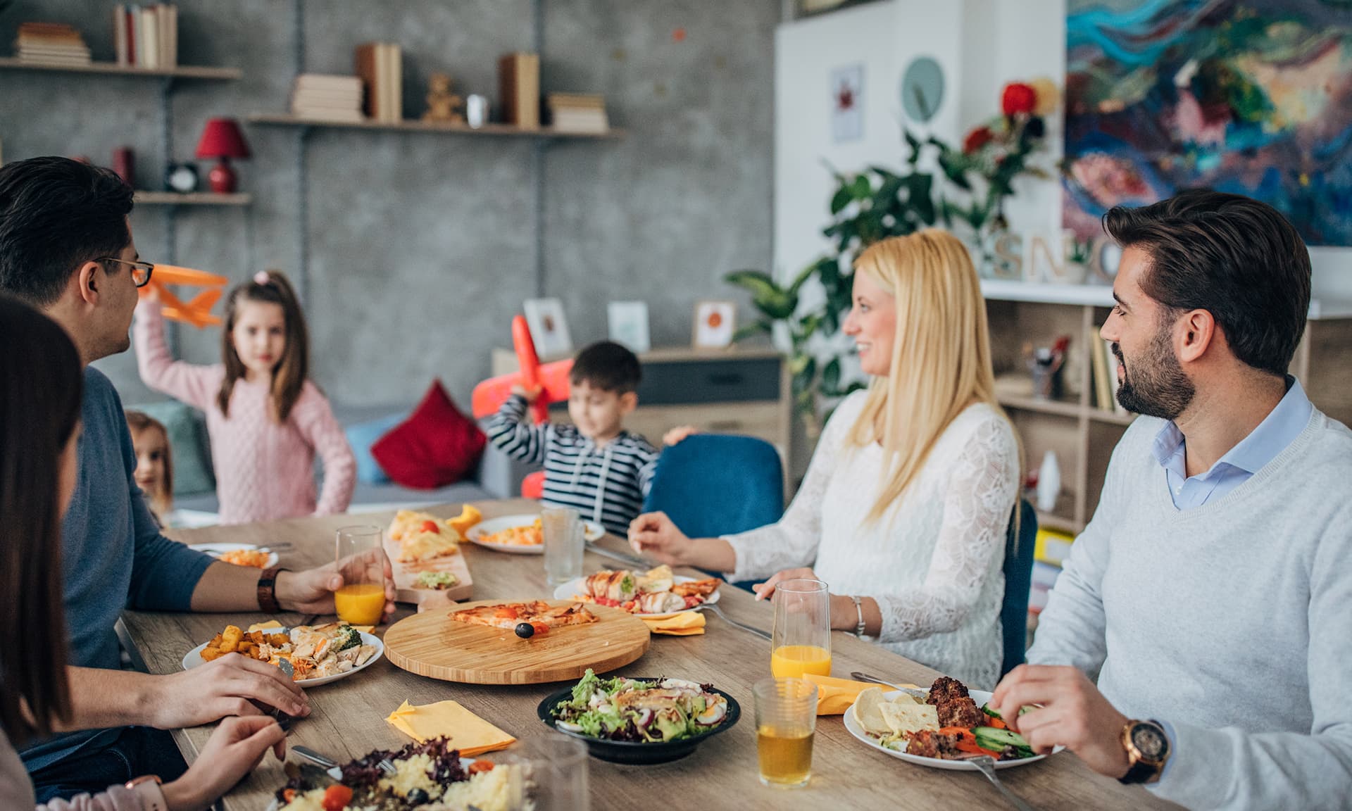 Two couples having a meal with kids in the background.