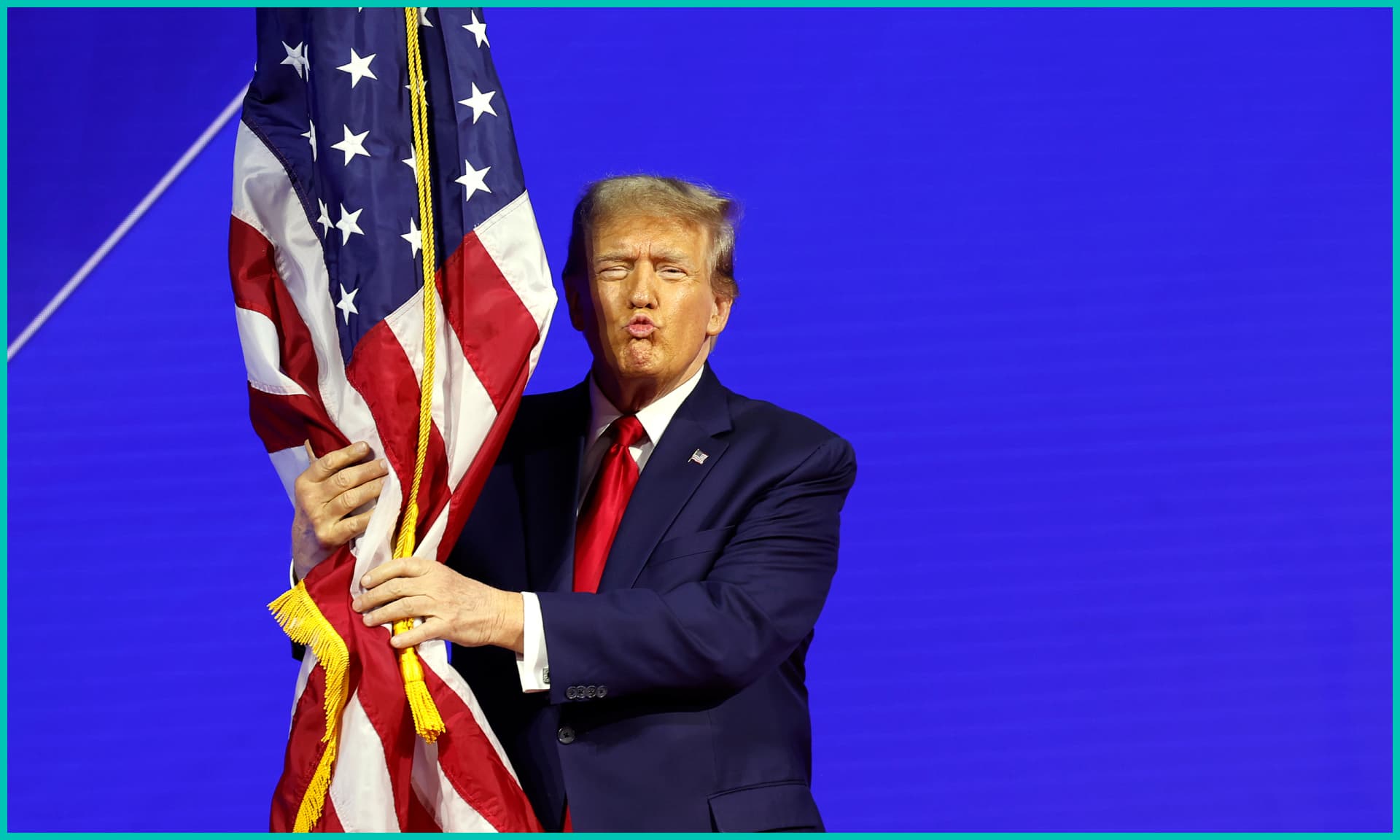 Republican presidential candidate and former U.S. President Donald Trump hugs an American flag as he arrives at the Conservative Political Action Conference
