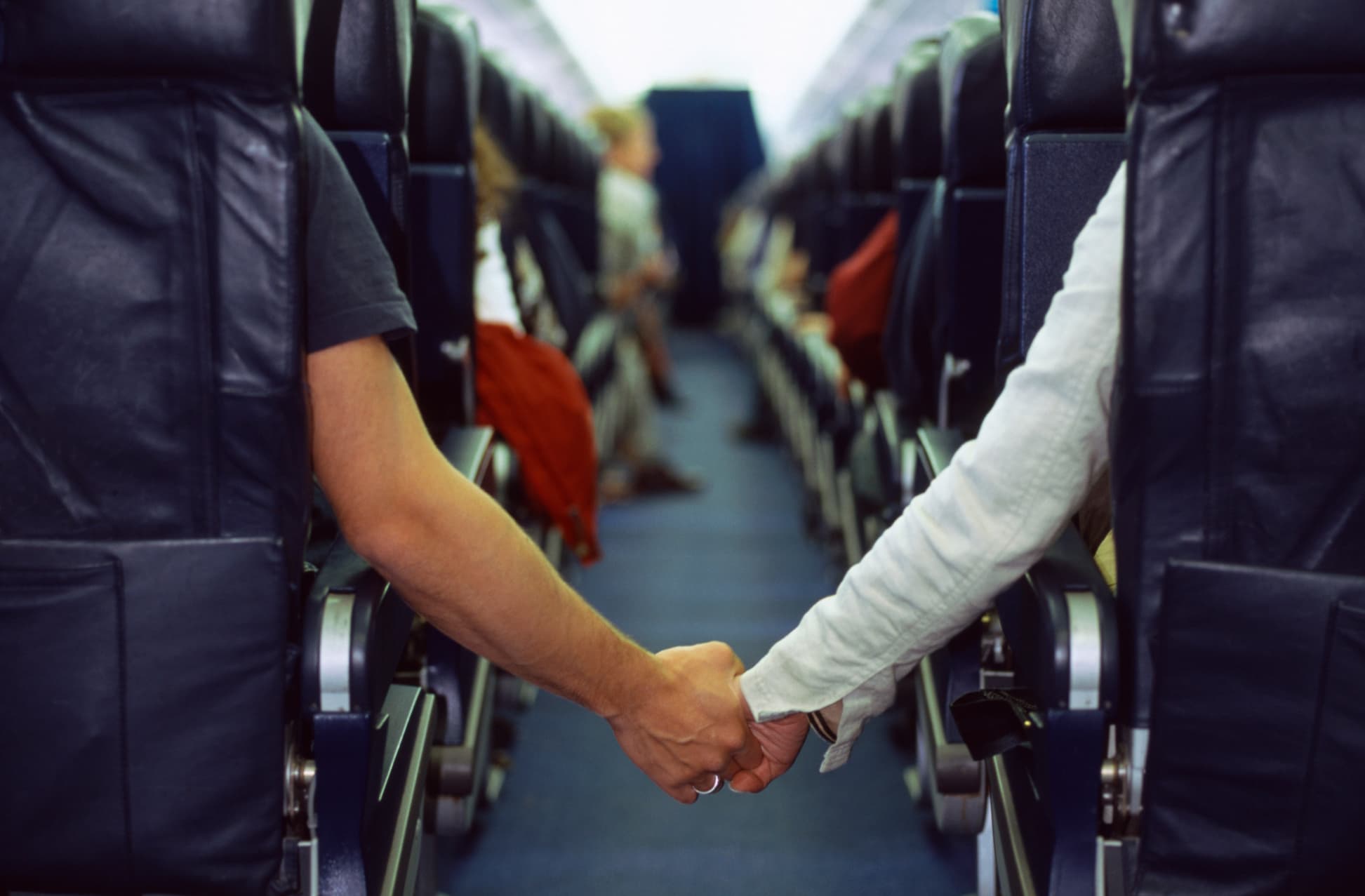 Couple holding hands across airplane aisle