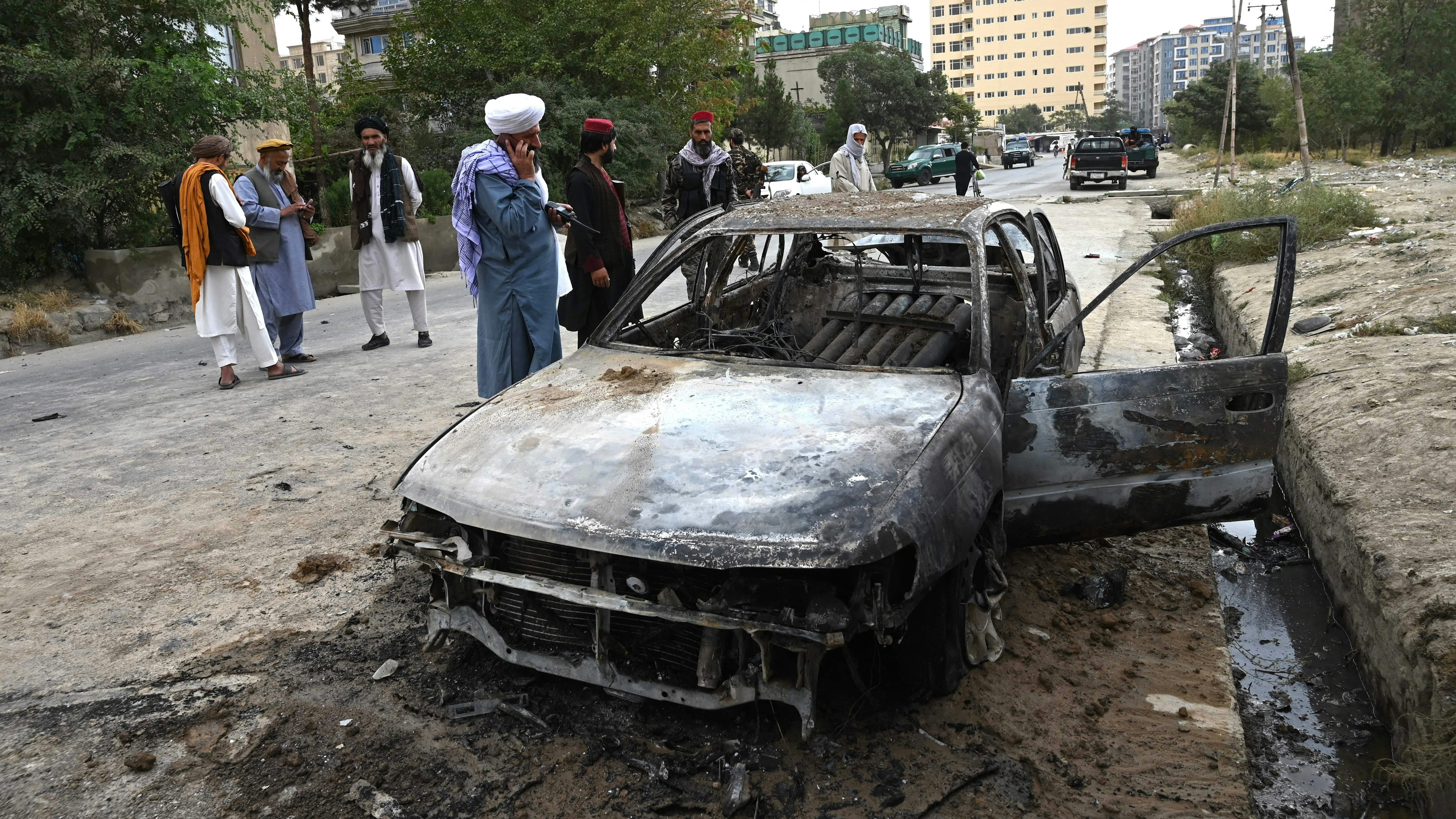 Taliban fighters investigate a damaged car after multiple rockets were fired in Kabul