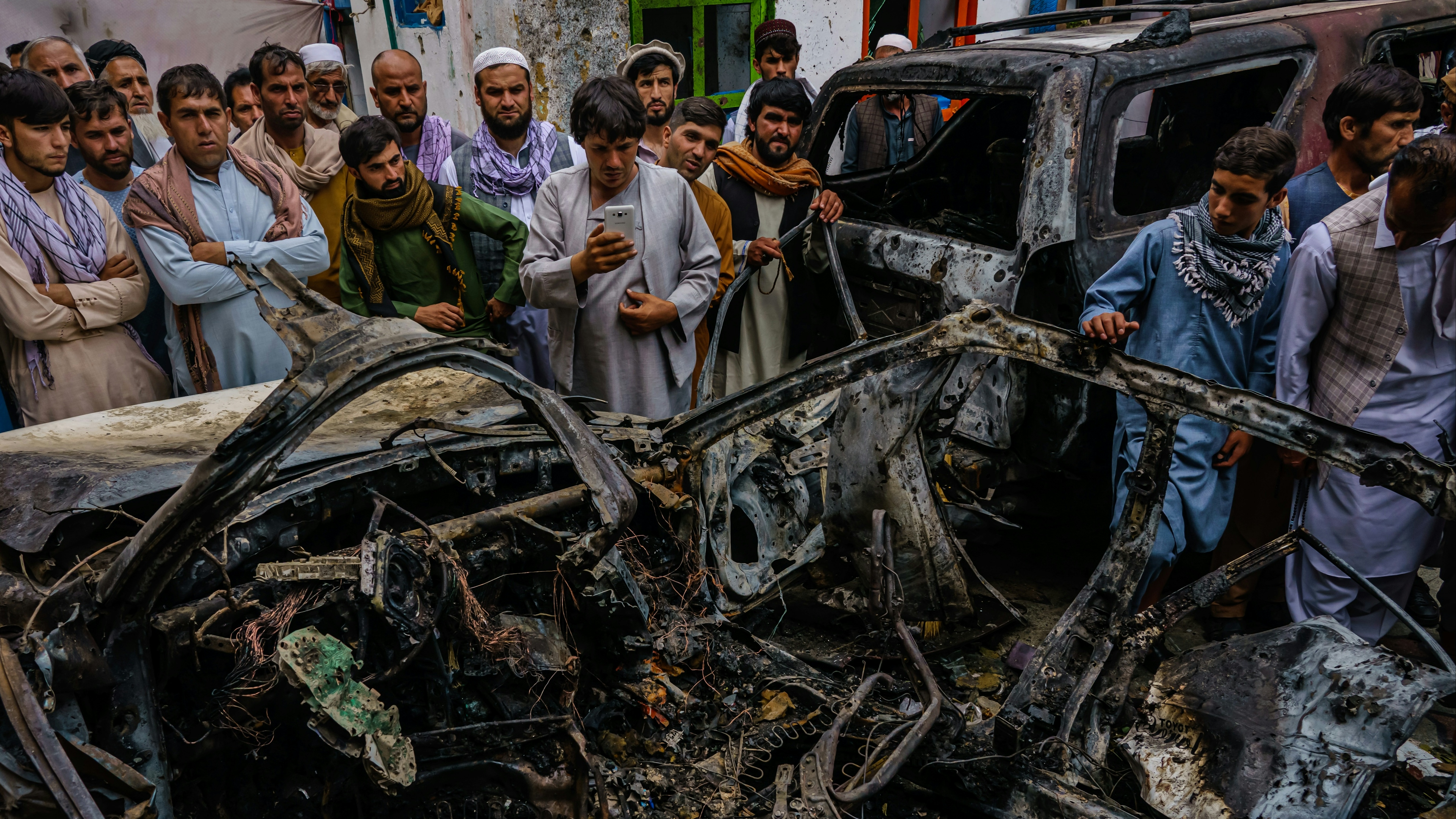 Relatives and neighbors gathered around the incinerated husk of a vehicle targeted and hit by an American drone strike, in Kabul, Afghanistan.