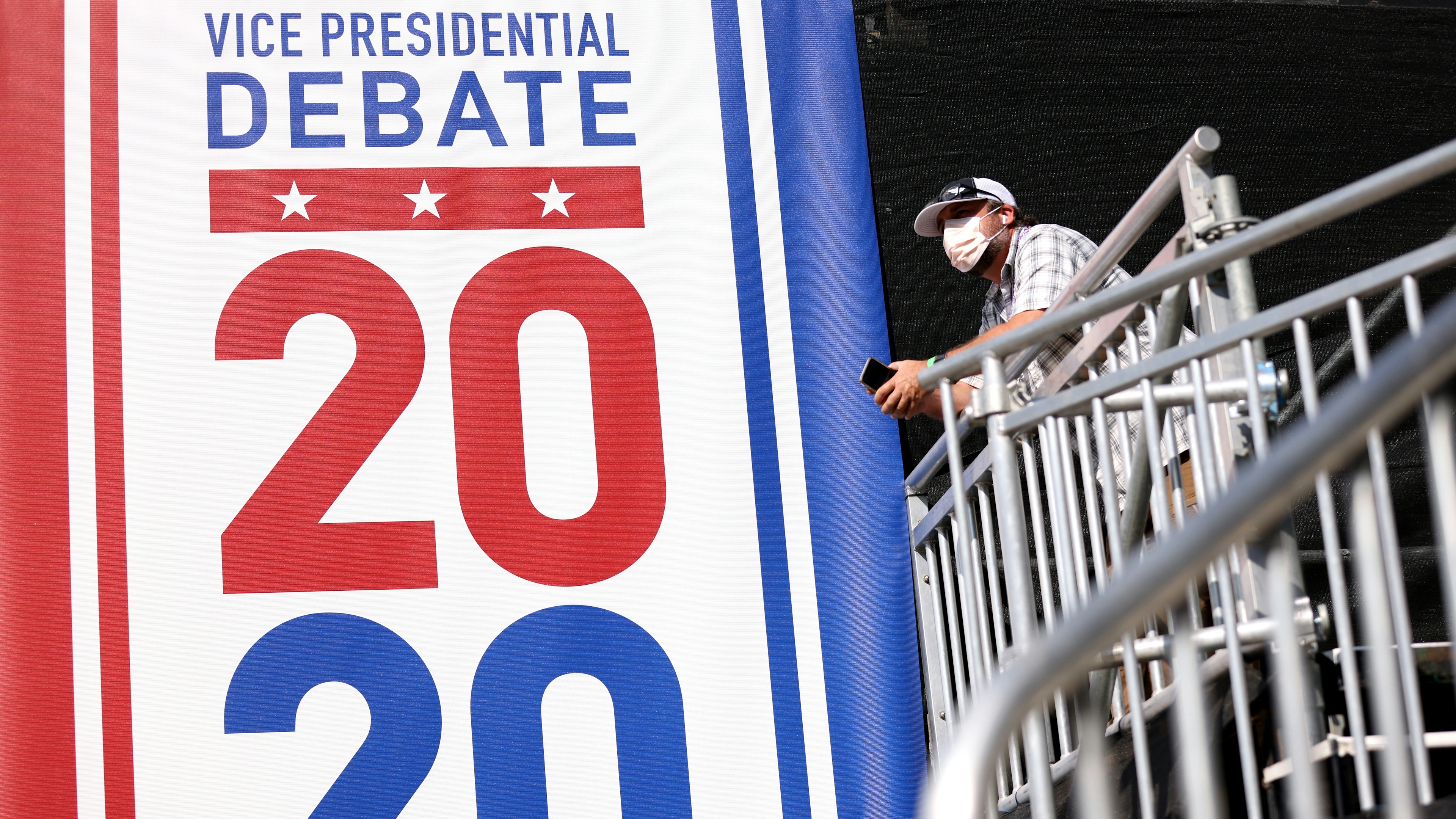 A worker stands next to a sign that reads "Vice Presidential Debate 2020" 