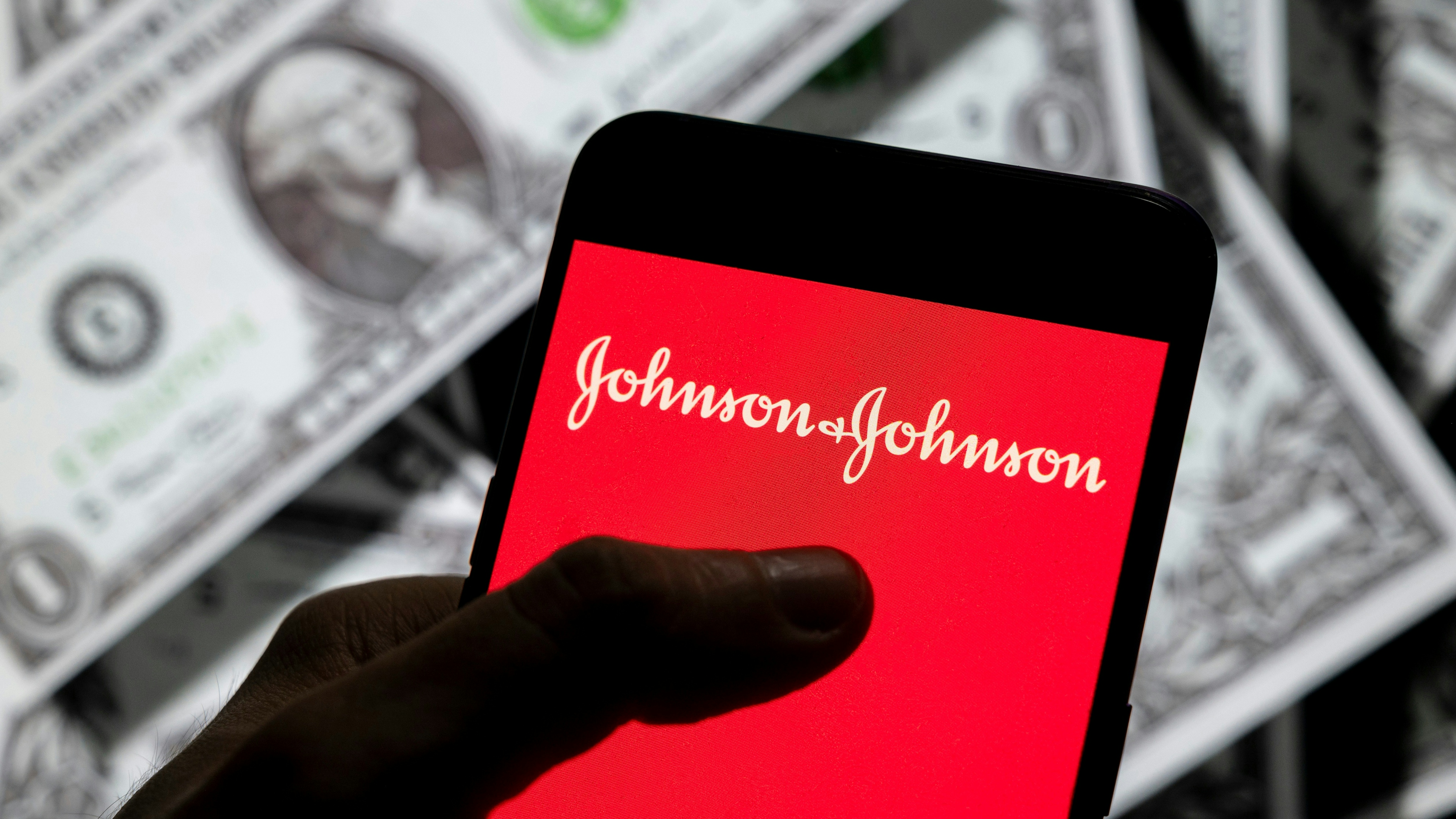 In this photo illustration, the American multinational medical devices and pharmaceutical company Johnson & Johnson logo seen on an Android mobile device screen with the currency of the United States dollar icon, $ icon symbol in the background. 