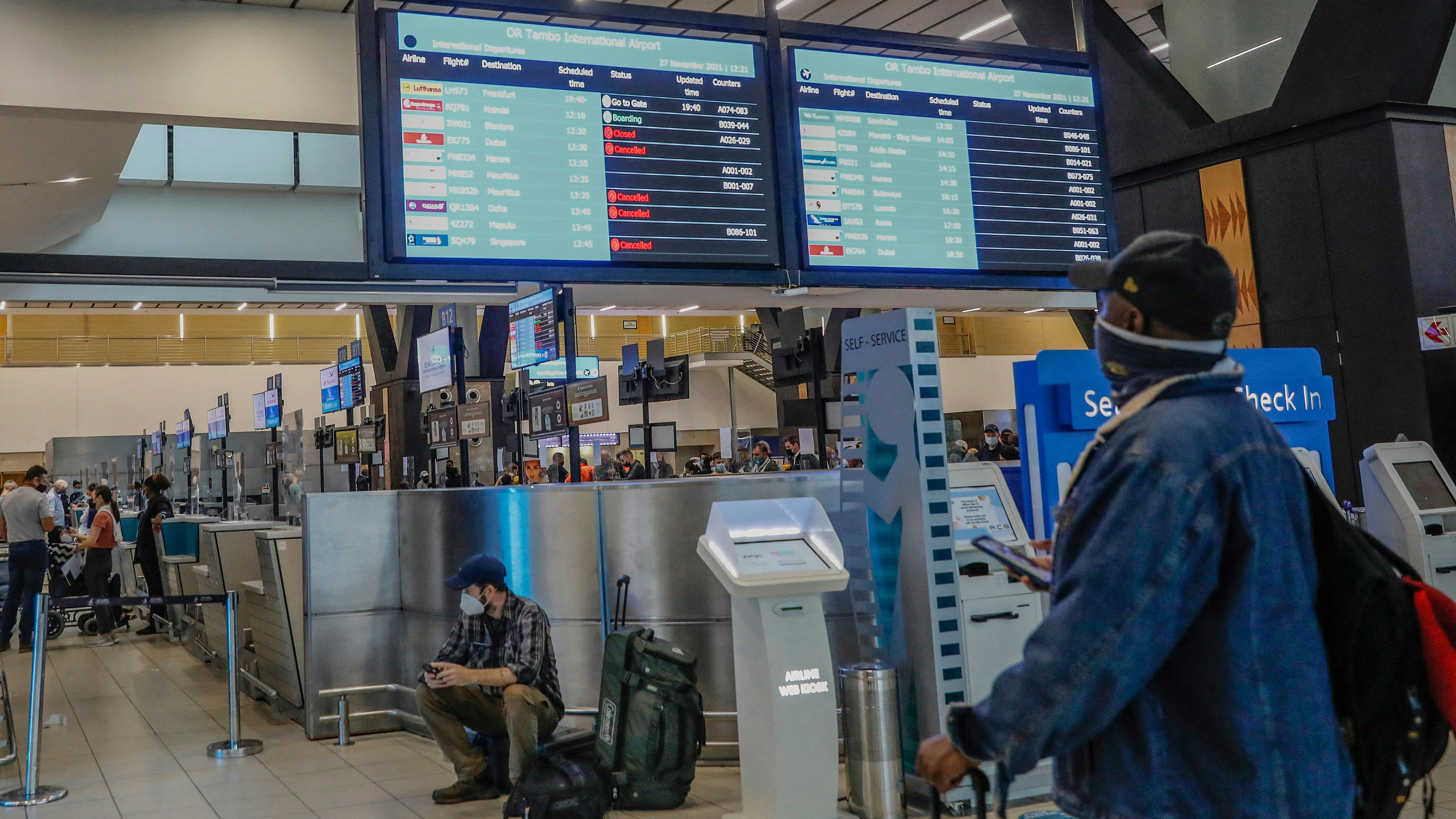 A passenger holds his mobile phone while looking at an electronic flight notice board displaying cancelled flights at OR Tambo International Airport in Johannesburg after several countries banned flights from South Africa following the discovery of Omicron
