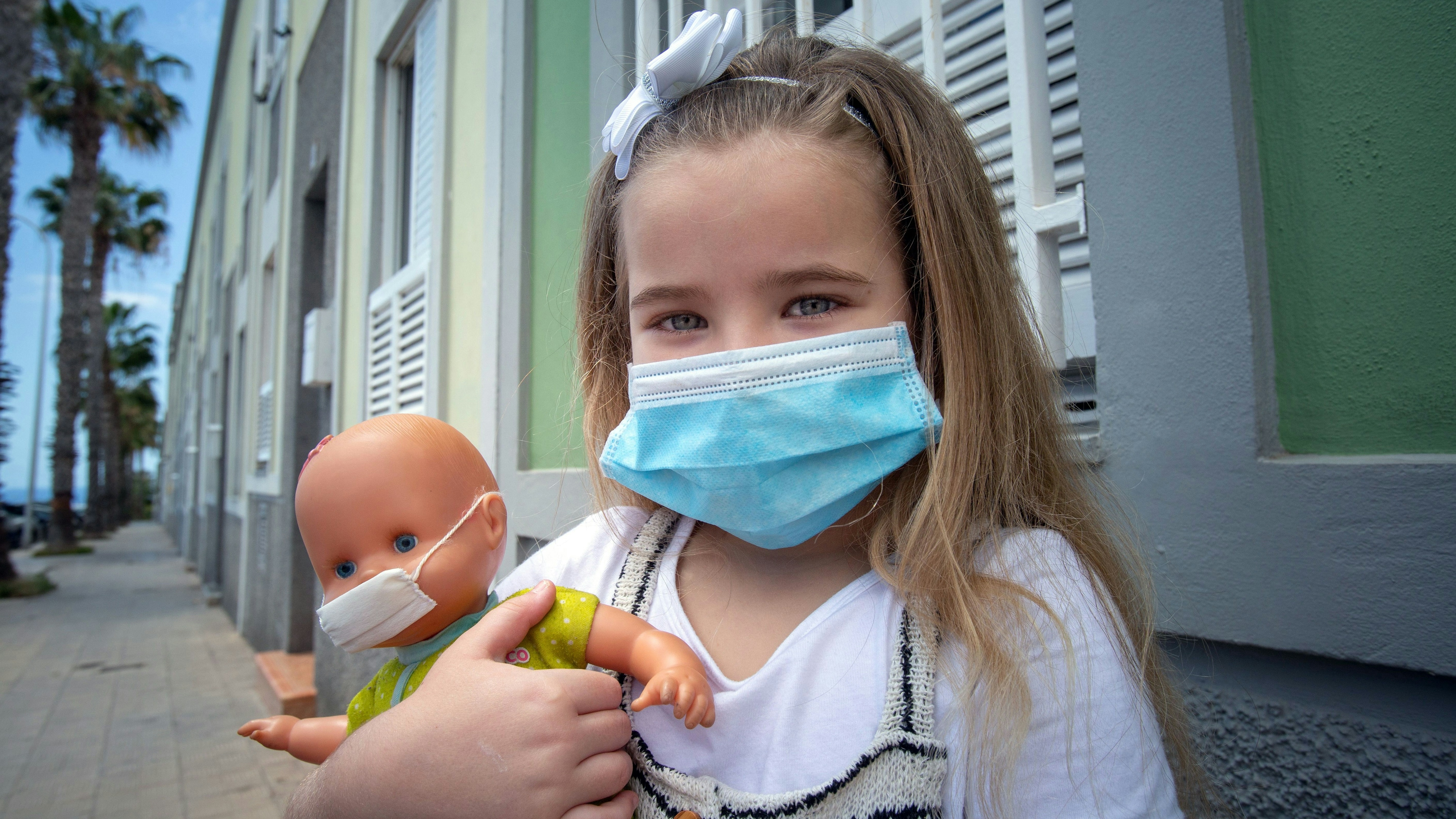 Girl and her doll pose wearing a face mask.
