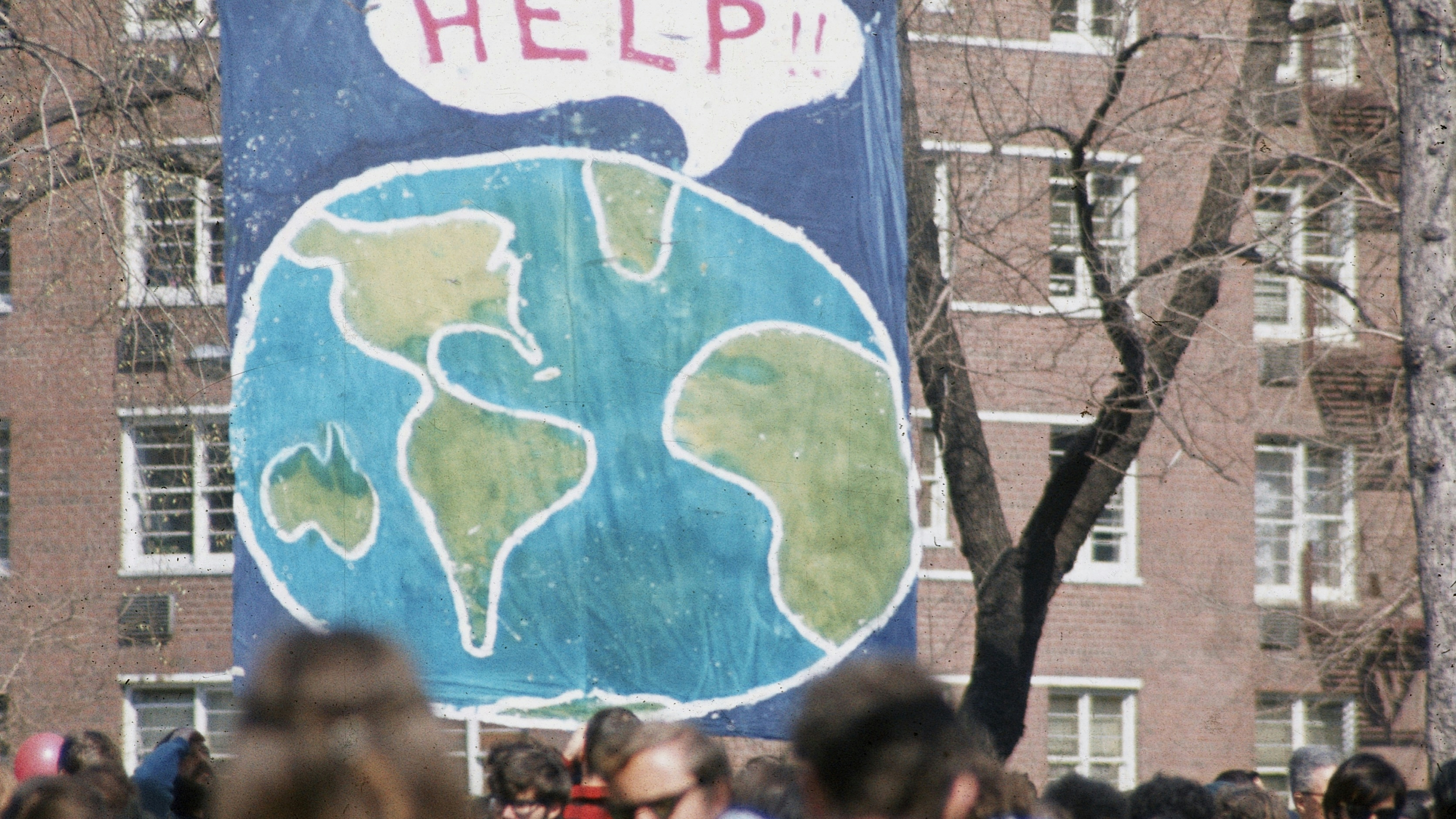 A crowd of people gather near a large poster that shows a speach bubble from planet Earth that reads 'Help!!', on the occaision of the first Earth Day conservation awareness celebration, New York, New York, April 22, 1970. 