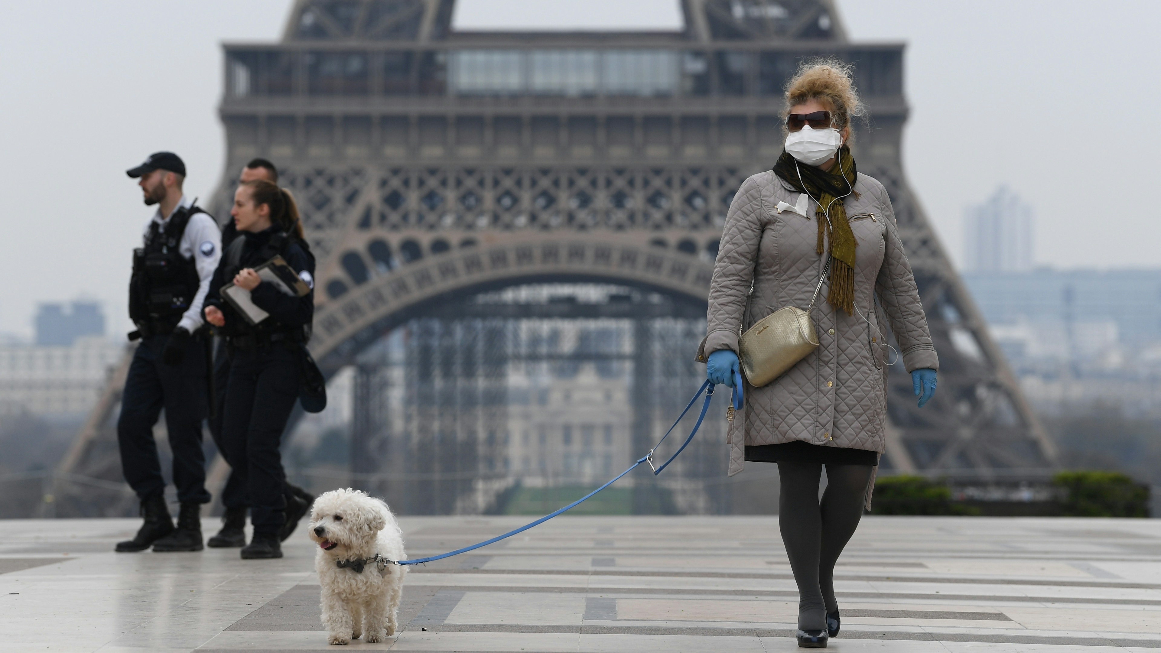 A woman wears protective gloves and a mask near the Eiffel Tower