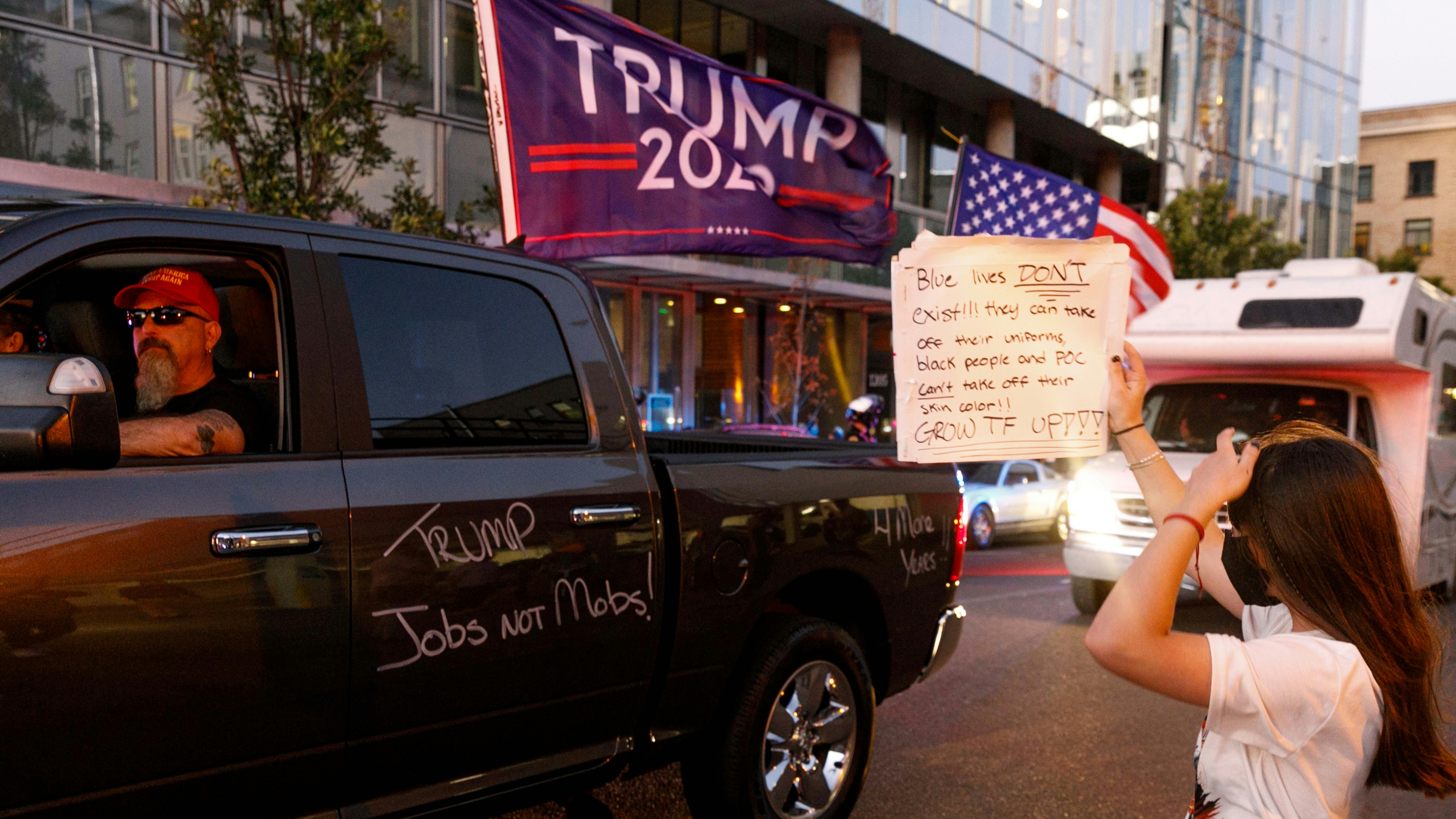 A BLM protester block Pickup trucks and cars full of flag-waving Donald Trump supporters