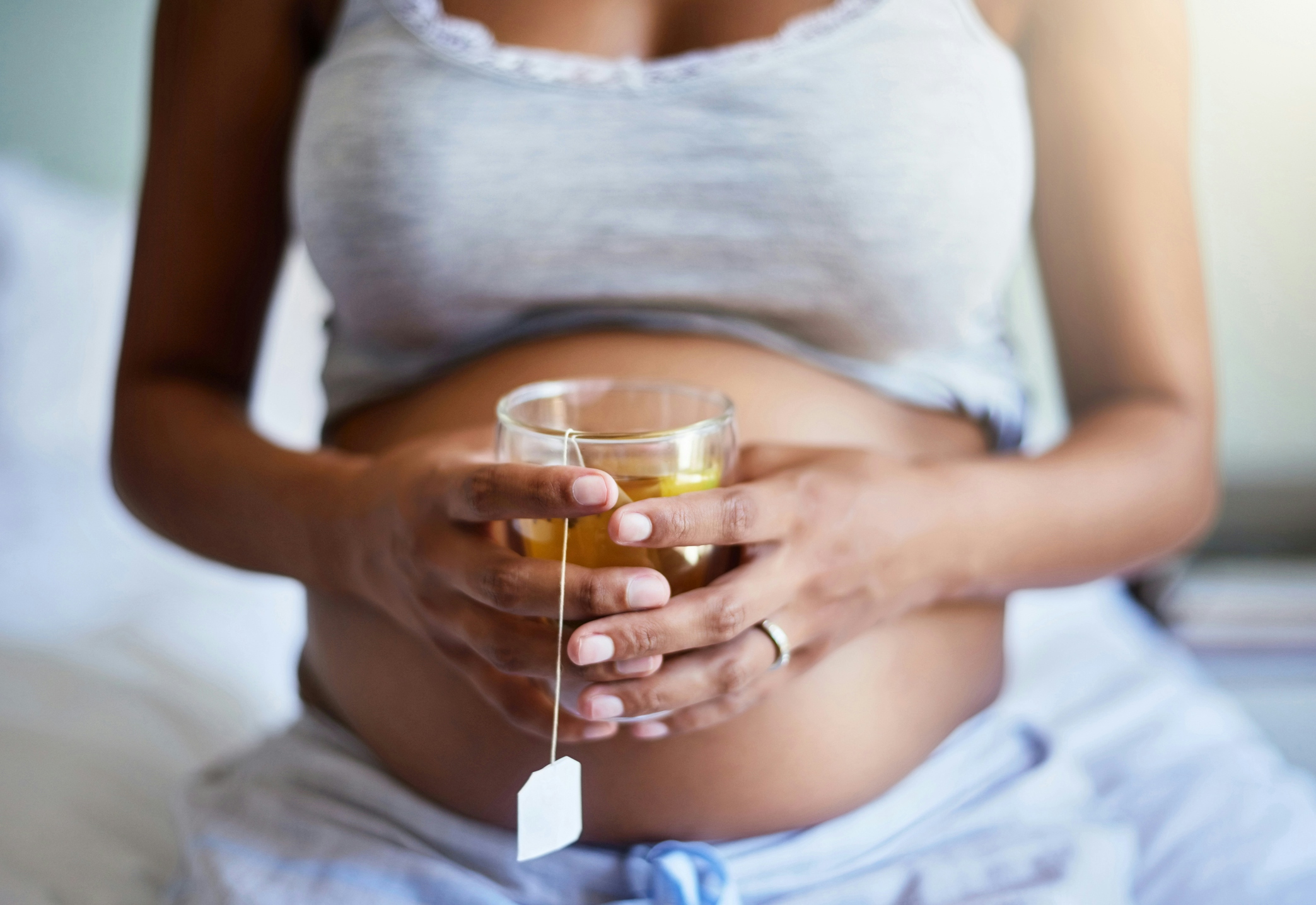 Pregnant woman holding a clear cup of tea in front of her belly