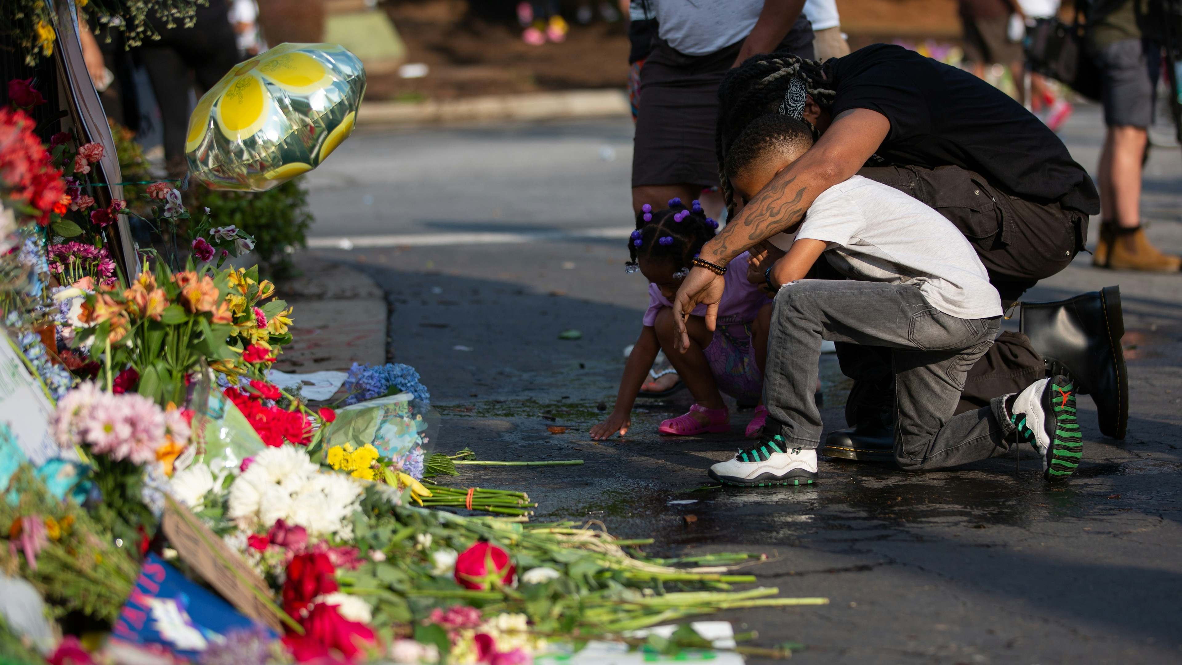 A man and two children kneel at the memorial of Rayshard Brooks.