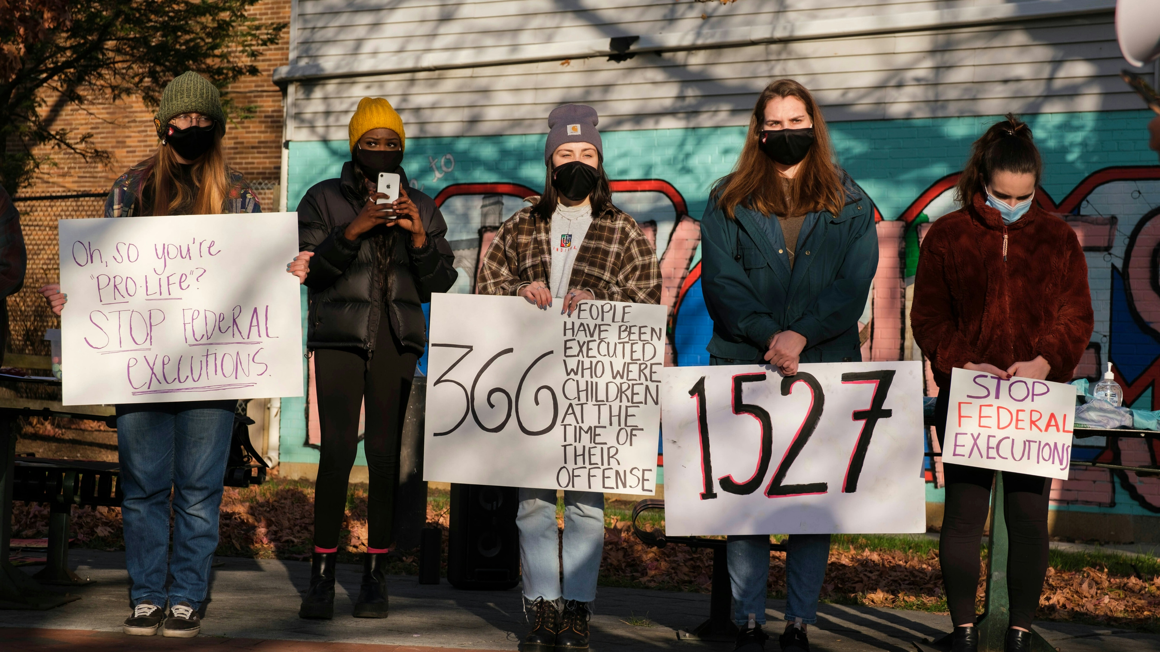 College students and community members wearing face masks hold placards while gathering in Peoples Park to protest against the death penalty.