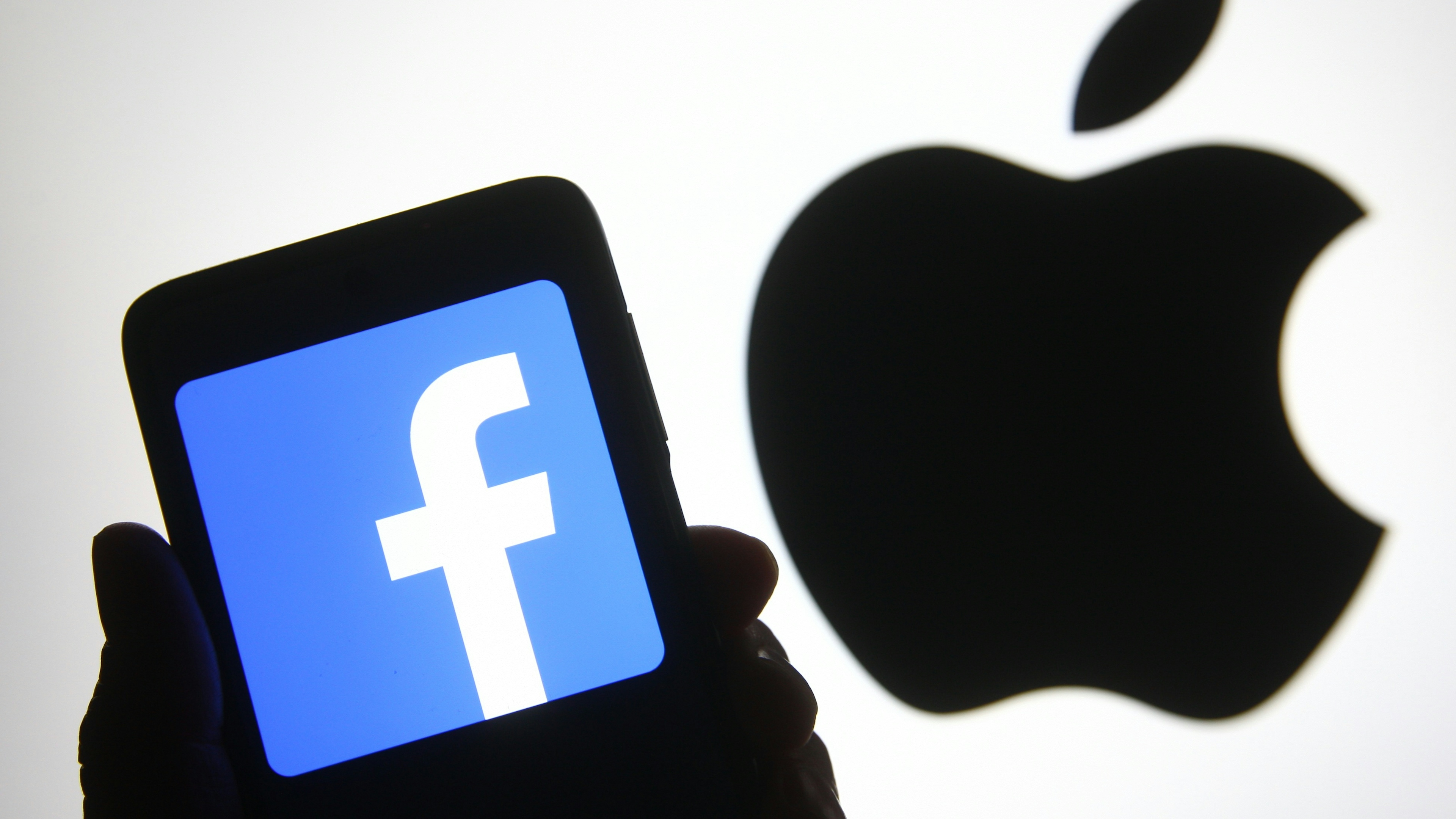 In this photo illustration, the Facebook logo seen displayed on a smartphone in front of an Apple logo.