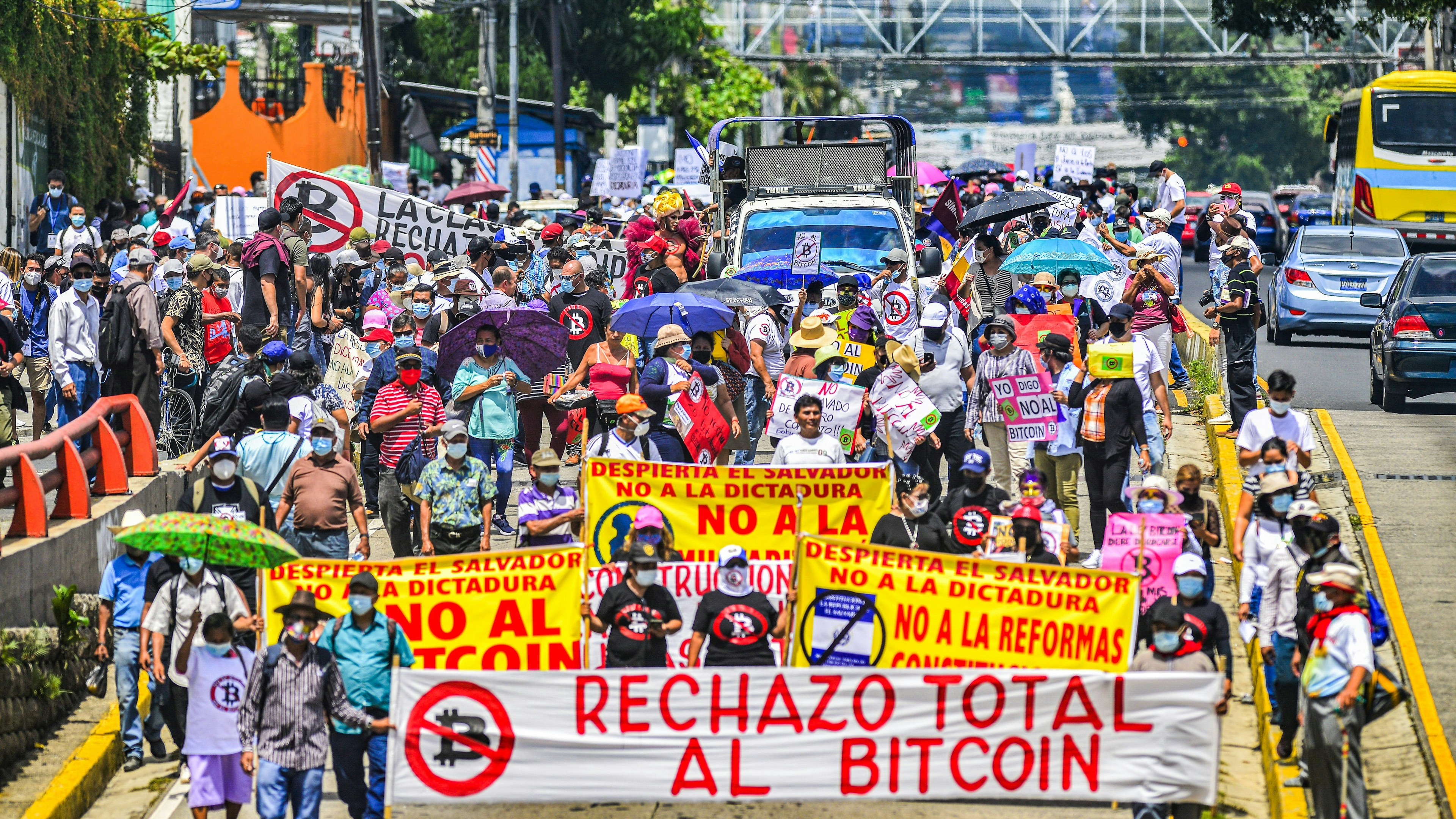 Demonstrators march while holding anti-bitcoin signs during the protest march in San Salvador.