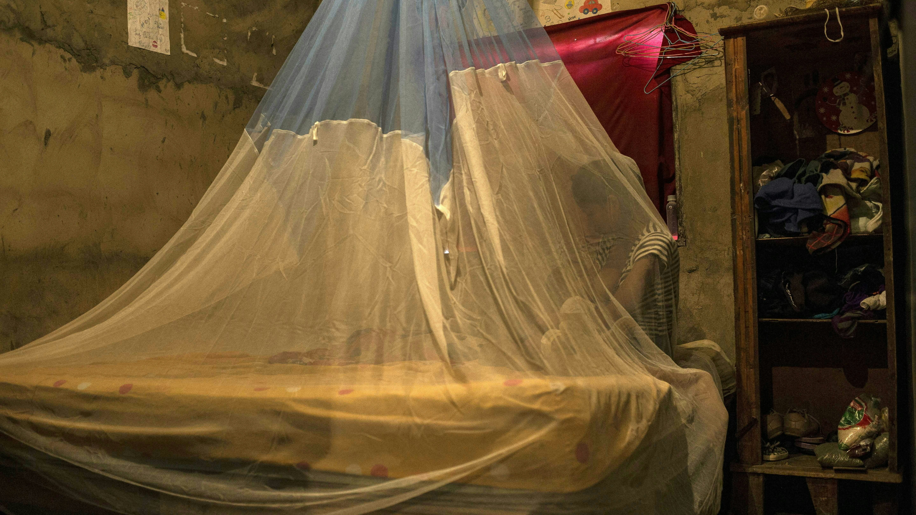 A woman rests wrapped in a mosquito net to protect herself from mosquitos which can transmit malaria 
