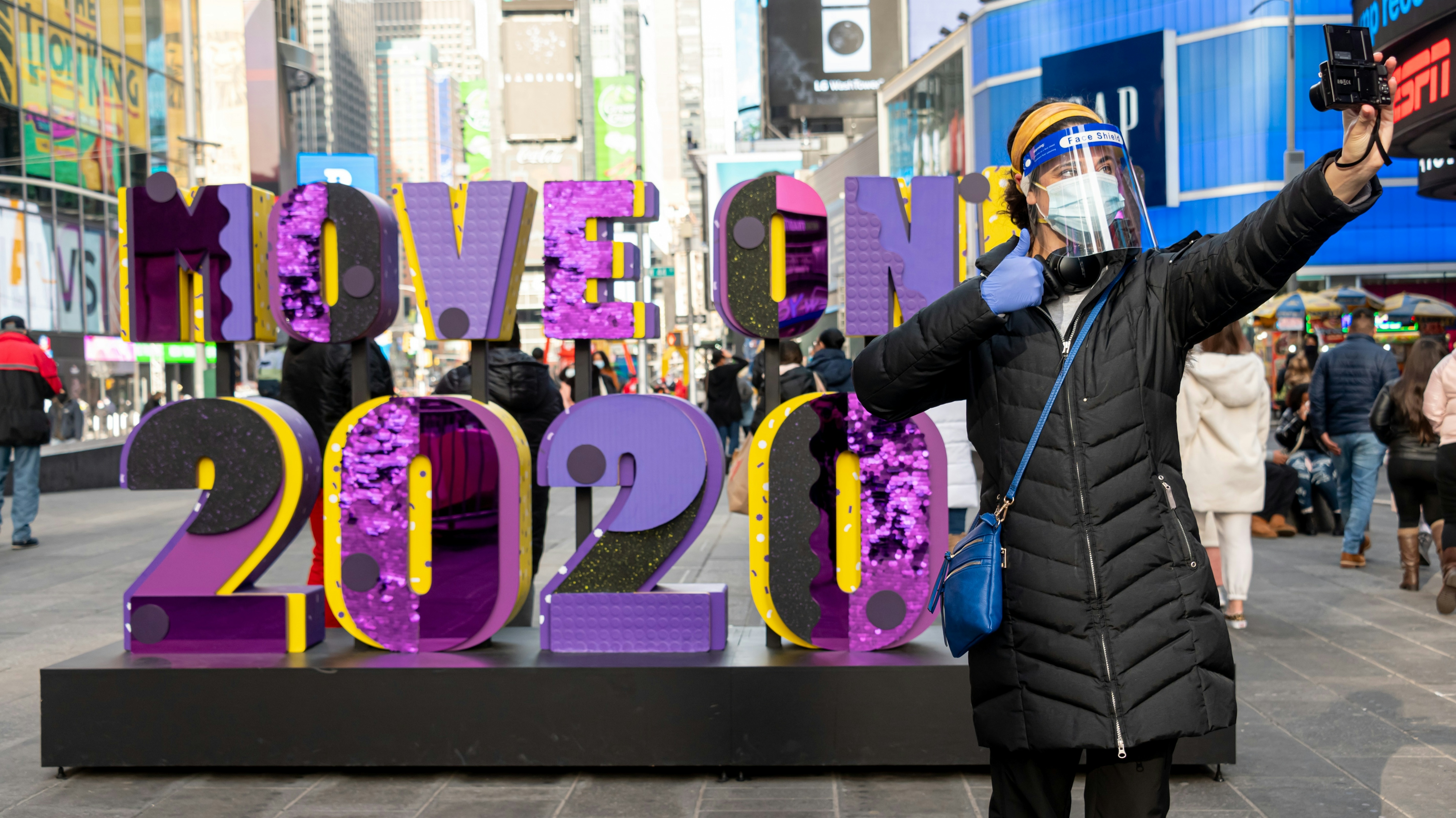 Woman stands in front of sign that says "Move On 2020" in Times Square.