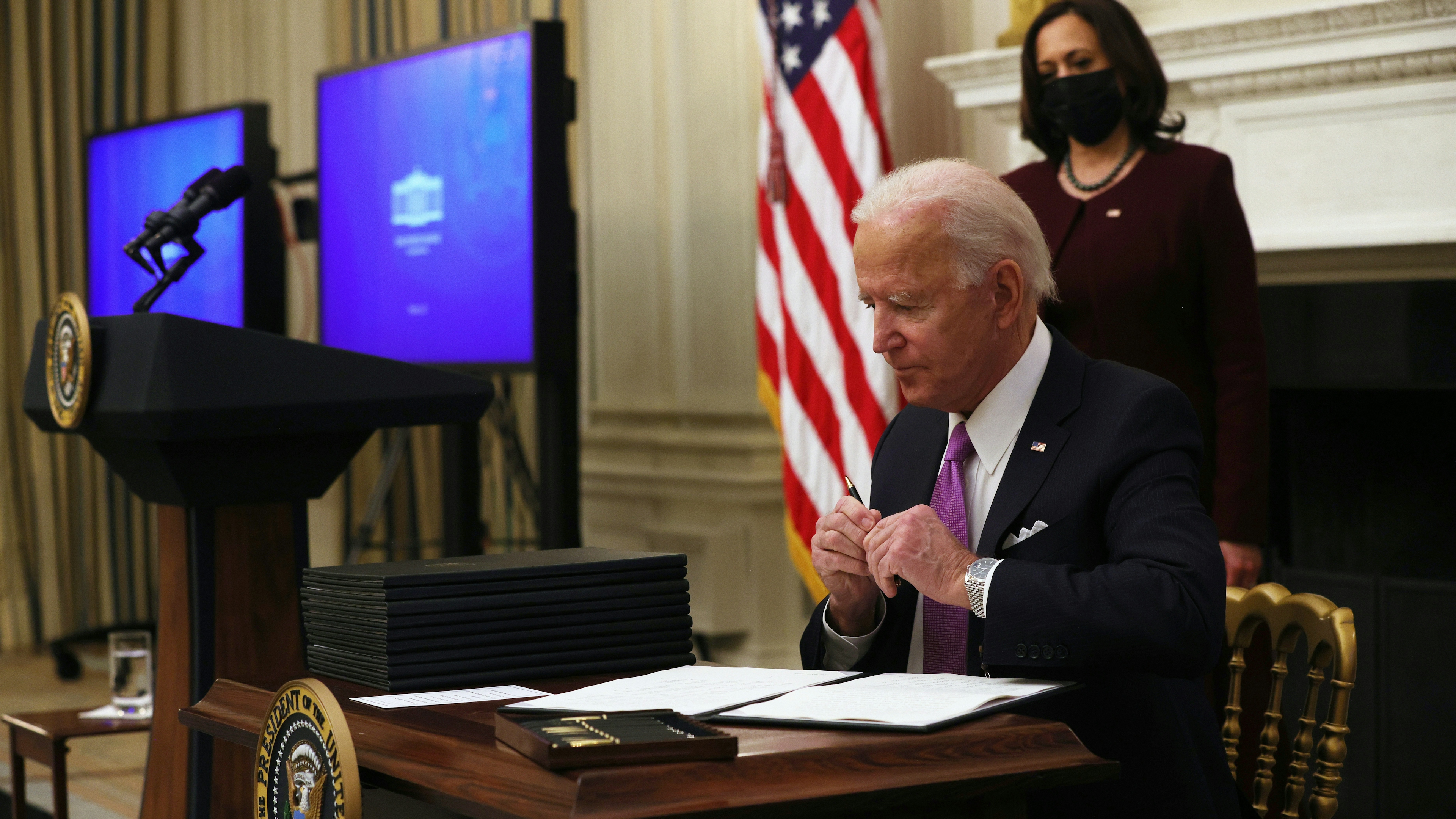 U.S. President Joe Biden signs executive orders as Vice President Kamala Harris looks on during an event at the State Dining Room of the White House January 21, 2021.