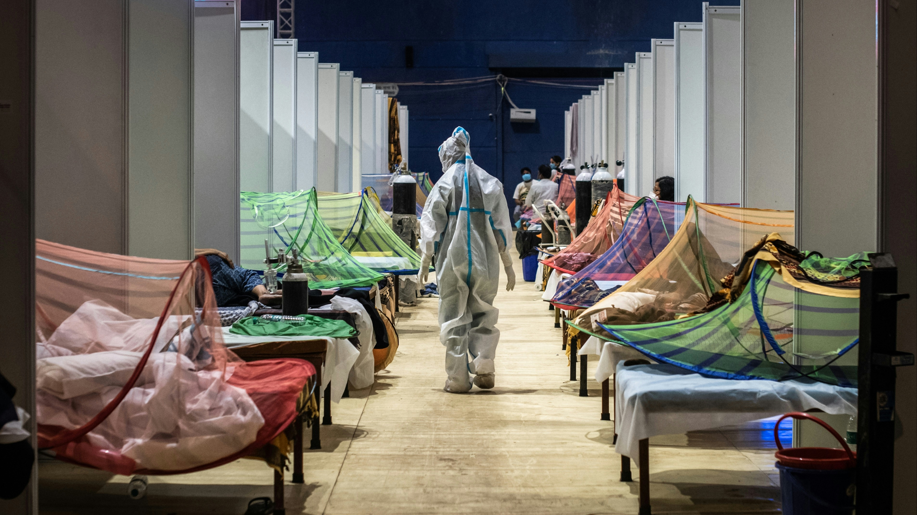 A medical worker in PPE observes patients who have been infected by Covid-19 inside a makeshift covid care facility in a sports stadium at the Commonwealth Games Village in New Delhi on May 02, 2021.